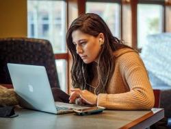 photo of white college aged woman working on laptop with headphones