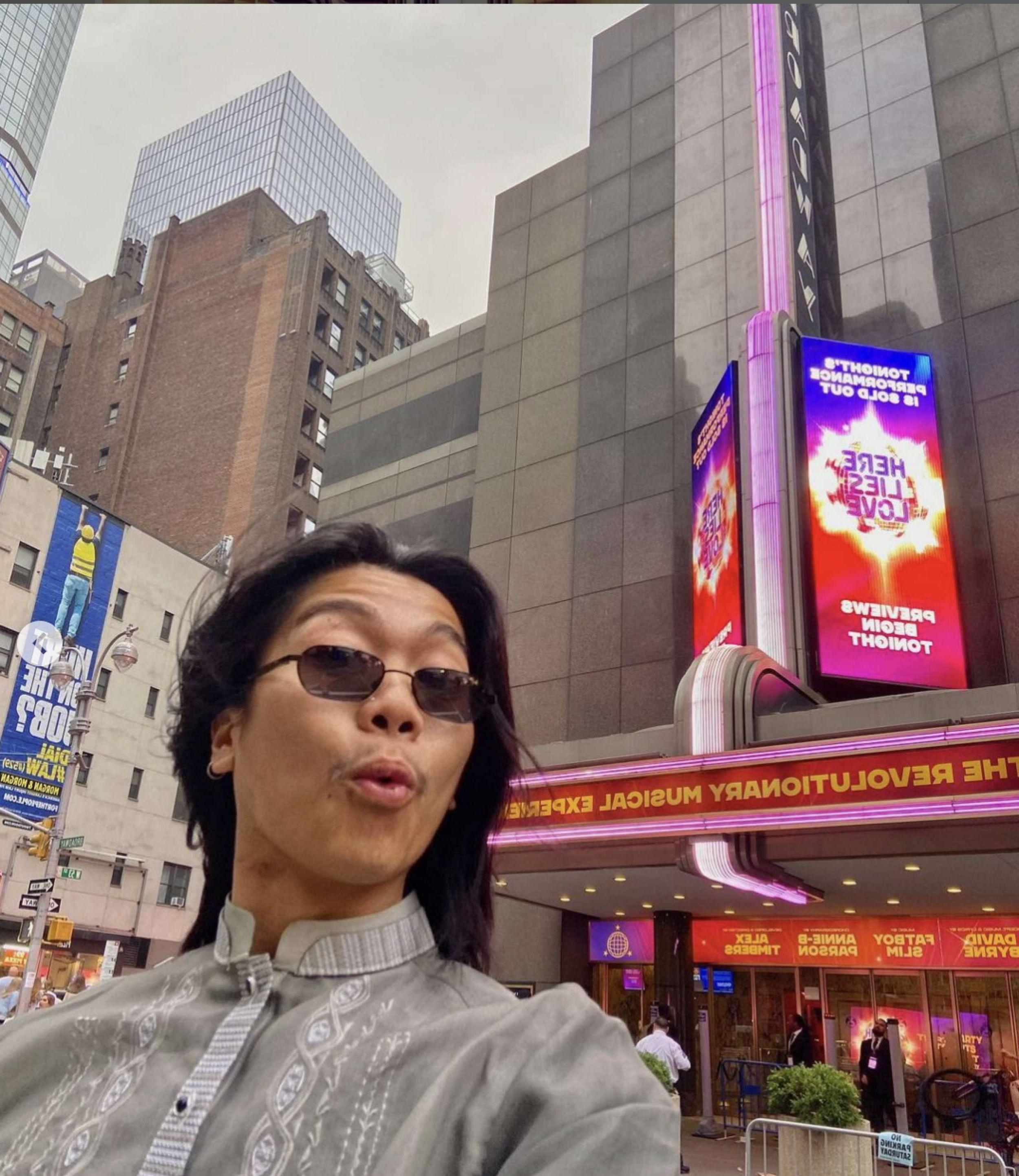 A young man in sunglasses in front of a Broadway theater.