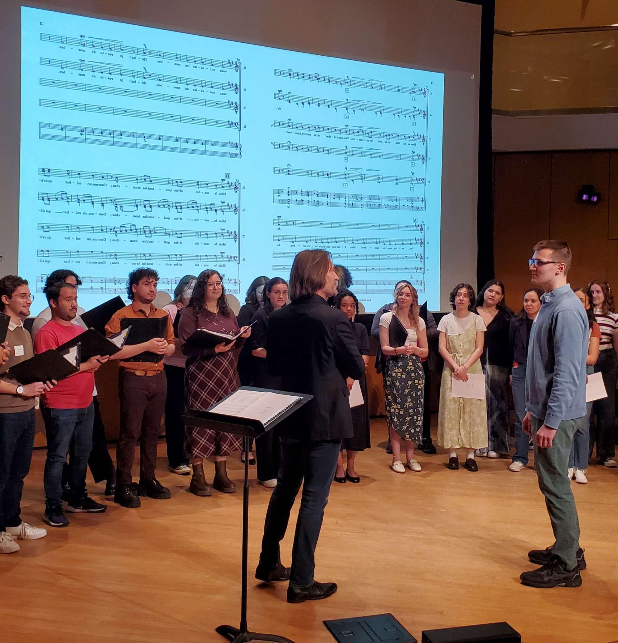 Singers stand in front of a projection of sheet music.