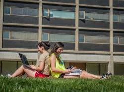 Two students sitting back to back outside of Blanton Hall in the grass.